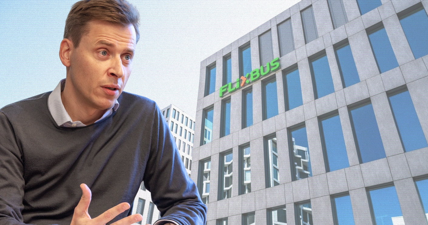 Mann im grauen Pullover spricht vor einem modernen Gebäude mit der Aufschrift "FLIXBUS" in grüner Schrift.