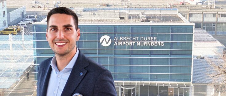 Mann in Anzug vor dem Albrecht Dürer Flughafen Nürnberg, moderne Architektur im Hintergrund.