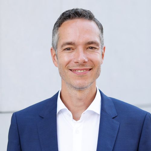 Porträt von Sebastian Rudolph, Kommunikationschef von Volkswagen, in einem blauen Anzug mit lächelndem Gesicht.