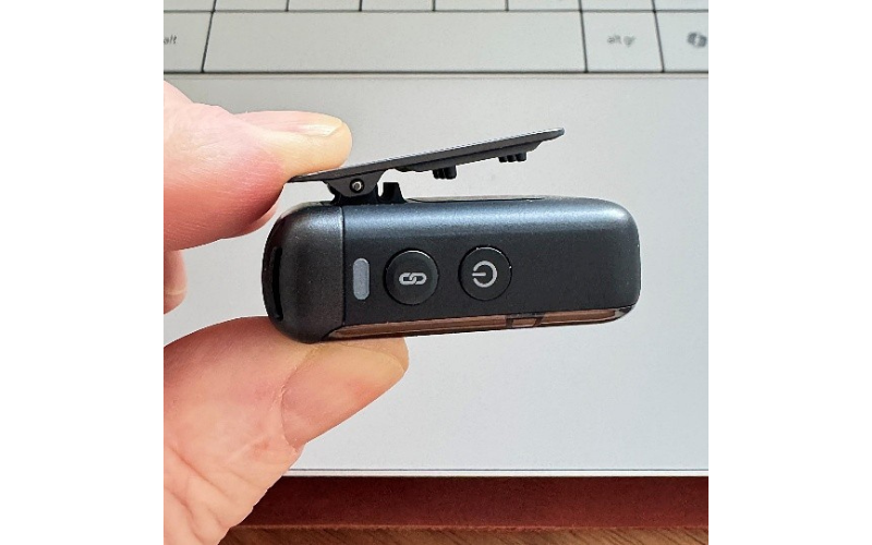 Hand hält ein schwarzes Mikrofon mit zwei Tasten vor einem Laptop.