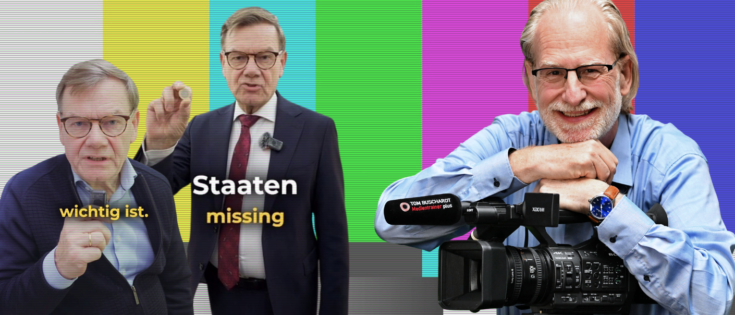 Zwei Männer in Anzügen vor buntem Hintergrund, einer hält einen Finger hoch, der andere steht mit einem Mikrofon.