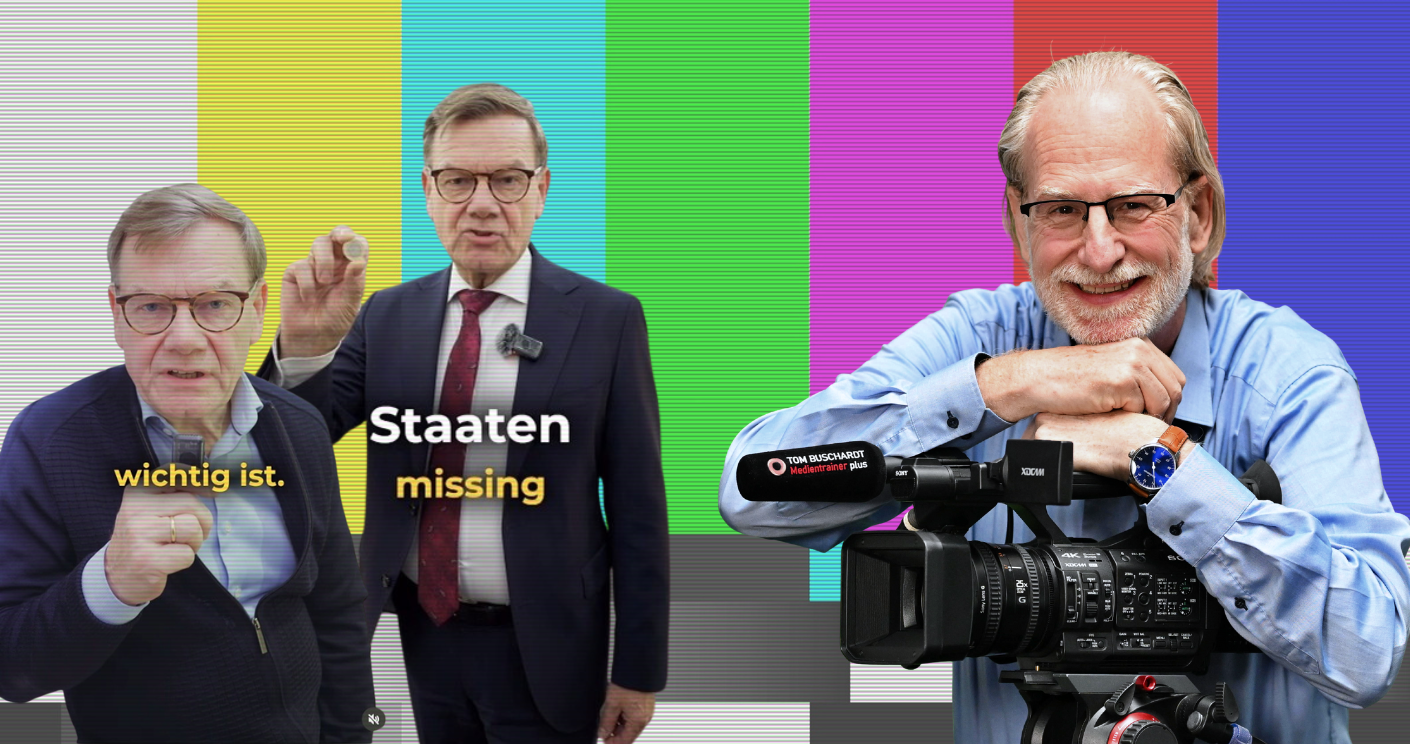 Zwei Männer in Anzügen vor buntem Hintergrund, einer hält einen Finger hoch, der andere steht mit einem Mikrofon.