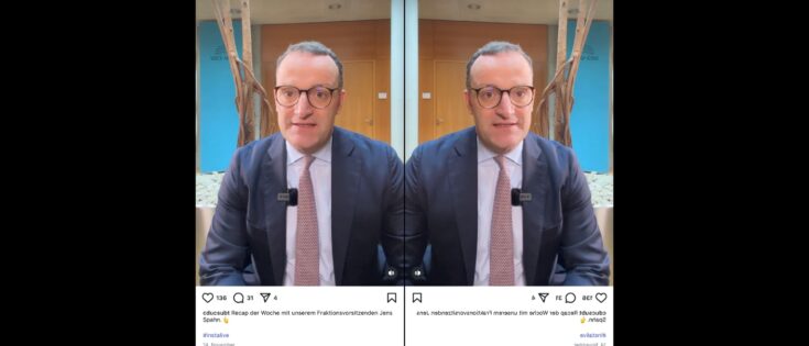 Jens Spahn sitzt in einem Konferenzraum, gespiegelt, mit Brille und Anzug, und lächelt in die Kamera.