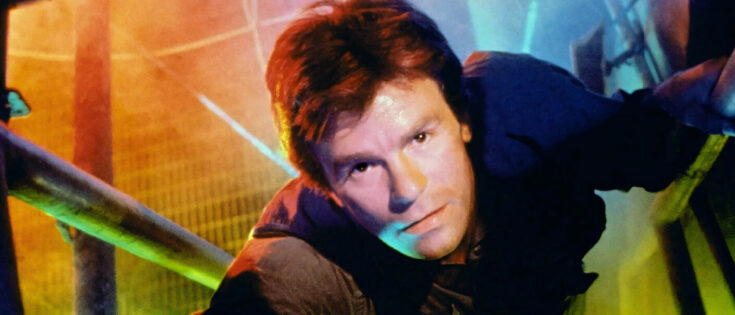 Mann in einem engen Raum, mit bunten Lichtern im Hintergrund, schaut direkt in die Kamera.