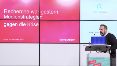 Mann spricht vor einem Bildschirm mit Präsentation über Medienstrategien gegen die Krise in Berlin, 2019.