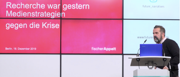 Mann spricht vor einem Bildschirm mit Präsentation über Medienstrategien gegen die Krise in Berlin, 2019.