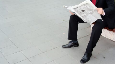 Geschäftsmann in Anzug sitzt auf einer Bank und liest eine Zeitung.