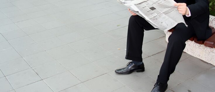 Geschäftsmann in Anzug sitzt auf einer Bank und liest eine Zeitung.
