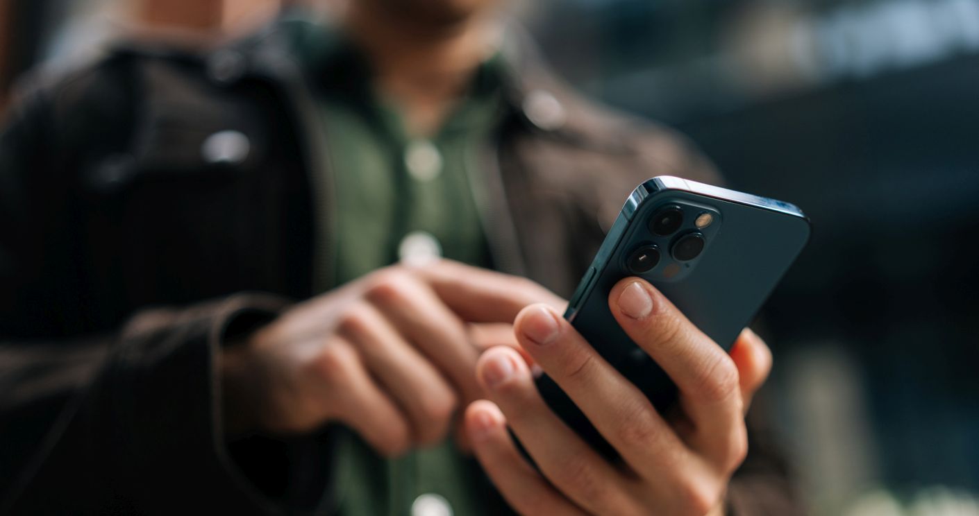 Nahaufnahme von Händen eines Mannes, der ein Smartphone hält und auf einer Stadtstraße das Internet durchsucht.