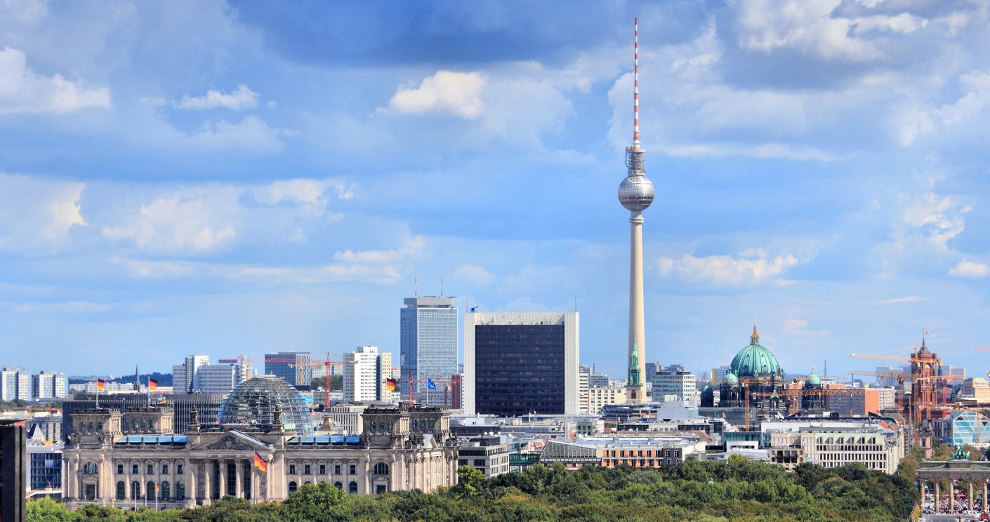 Skyline von Berlin mit dem Reichstag, Tiergarten und dem Fernsehturm vor einem bewölkten Himmel.