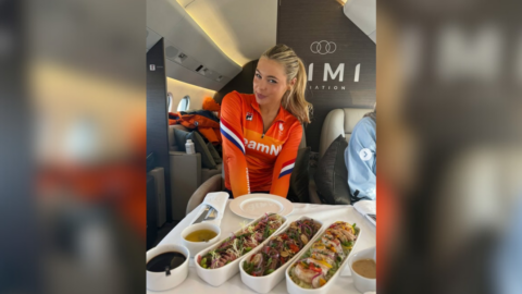 Frau in orangefarbener Sportkleidung sitzt in einem Flugzeug mit einem Tisch voller Sushi und Saucen.