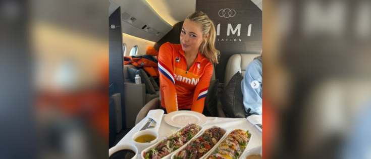 Frau in orangefarbener Sportkleidung sitzt in einem Flugzeug mit einem Tisch voller Sushi und Saucen.