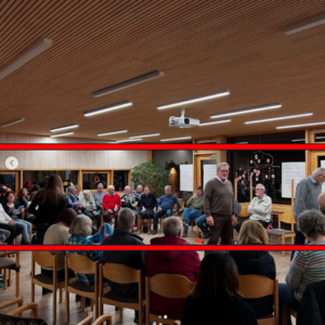 Gruppensitzung in einem hellen Raum mit Stühlen, Teilnehmern und einem Präsentationsprojektor.