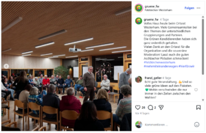 Menschen versammeln sich in einem Raum, diskutieren in Gruppen, Stühle sind um einen Tisch angeordnet.