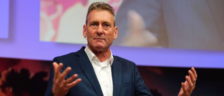 Mann in Anzug spricht auf einer Bühne, gestikuliert mit beiden Händen.