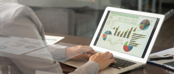 Frau tippt auf Laptop, während sie ein Finanzbericht-Diagramm mit Balken- und Kreisdiagrammen betrachtet.