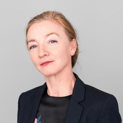 Porträt von Miriam Kahrmann in einem schwarzen Blazer vor einem grauen Hintergrund.
