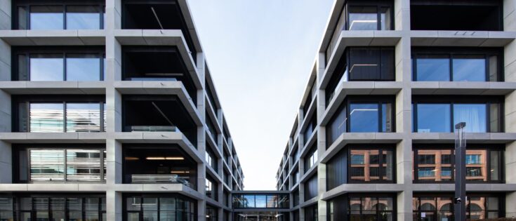 Moderne Gebäude mit großen Fenstern und klaren Linien, die einen offenen Innenhof umgeben.