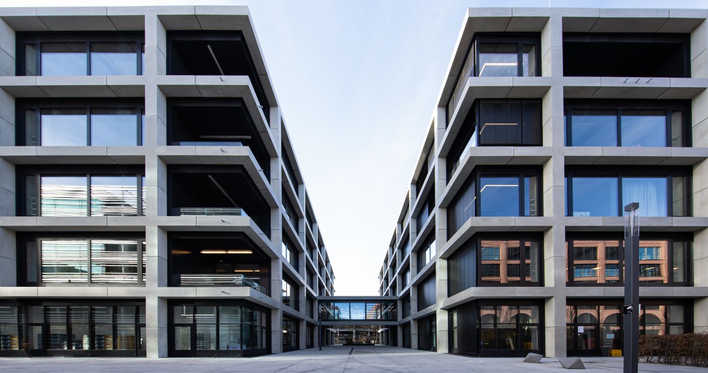 Moderne Gebäude mit großen Fenstern und klaren Linien, die einen offenen Innenhof umgeben.