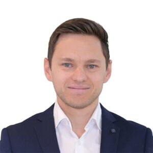 Porträt eines Mannes mit kurzem, braunem Haar, in einem dunklen Anzug und weißem Hemd, vor weißem Hintergrund.