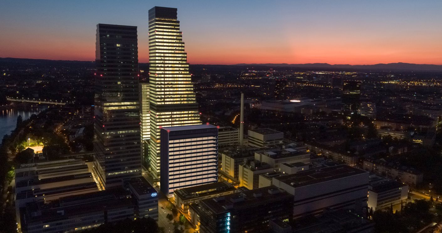 Nachtaufnahme der Roche-Gebäude in Basel, beleuchtet vor einem farbenfrohen Sonnenuntergang.