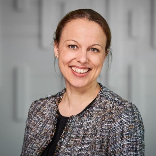 Porträt von Silke Amthauer, lächelnd, mit blauer Jacke vor einem neutralen Hintergrund.