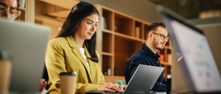 Diverse Teammitglieder arbeiten an Laptops in modernem Büro; eine Frau konzentriert sich auf ihre Aufgaben.