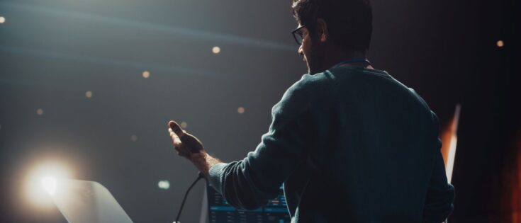 Junger Redner steht hinter einem Podium und präsentiert eine Rede.