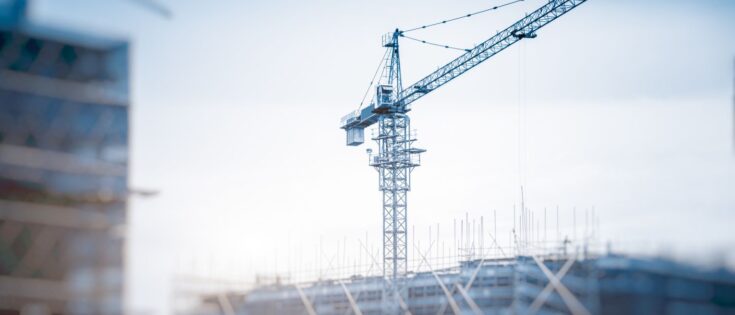 Blick von unten auf Kräne vor der Skyline von Shanghai, China, mit Bauarbeiten im Vordergrund.