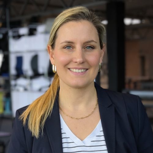 Porträt von Helena Mager mit blonden Haaren, lächelnd, in einem Blazer vor einem modernen Hintergrund.