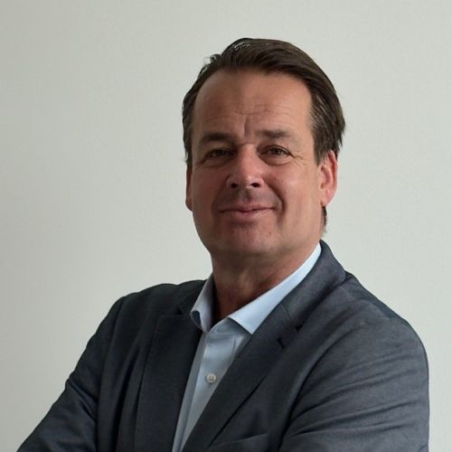 Henning Busch in einem grauen Anzug, lächelnd vor einem hellen Hintergrund, spricht für Genesis Motor Deutschland.