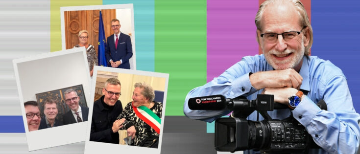 Ein Mann mit Brille lächelt, während er eine Kamera hält. Im Hintergrund sind bunte Streifen und Fotos von Personen.