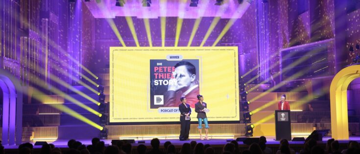 Verleihung des Podcast-Awards mit Bühne, Lichtern und Präsentation des Podcasts „Die Peter Thiel Story“.