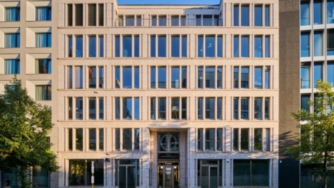 Moderne Bürogebäude mit Glasfassade und symmetrischer Anordnung der Fenster, umgeben von Bäumen.