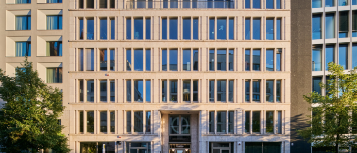 Moderne Bürogebäude mit Glasfassade und symmetrischer Anordnung der Fenster, umgeben von Bäumen.