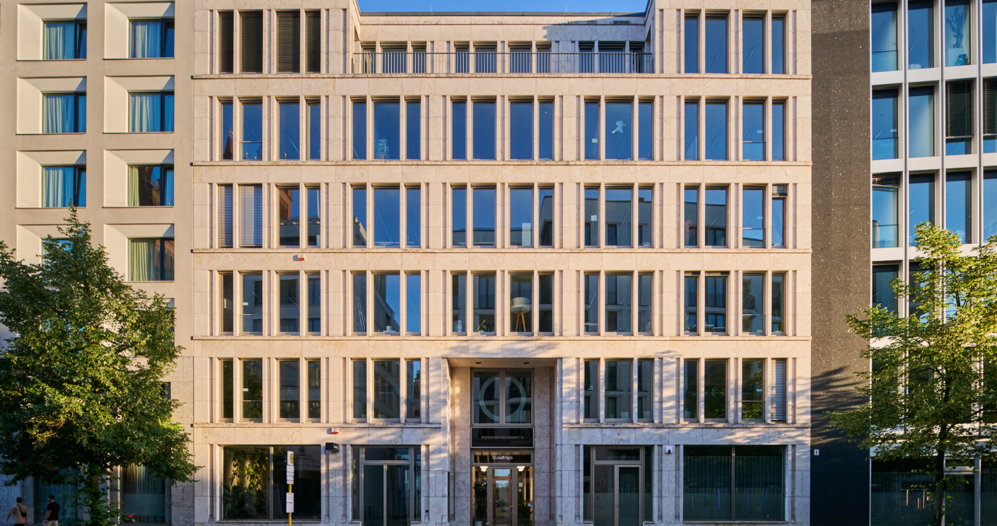 Moderne Bürogebäude mit Glasfassade und symmetrischer Anordnung der Fenster, umgeben von Bäumen.