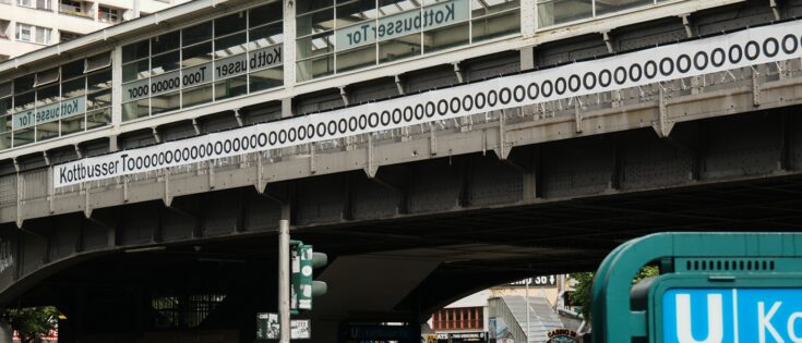 Urban scene in Berlin: a metal bridge with a 'Kottbusser Tor' banner and a blue U-Bahn sign in the foreground.