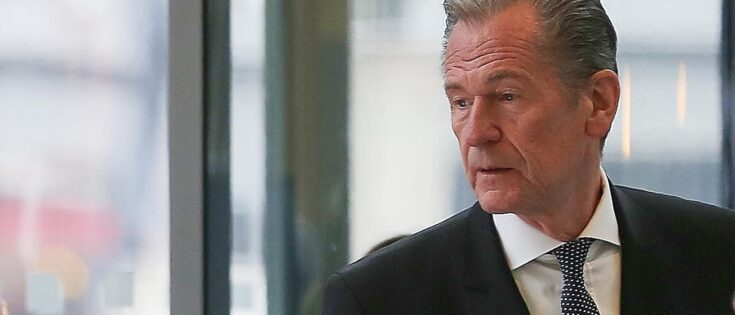 Mathias Döpfner in einem Anzug, steht in einem modernen Gebäude mit großen Fenstern.