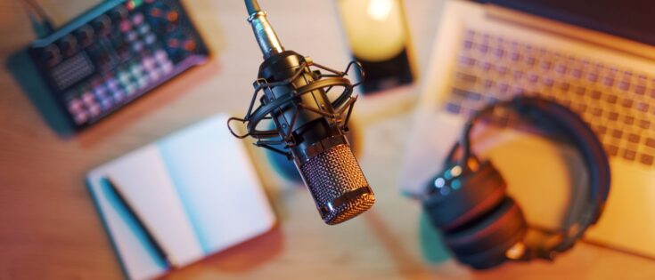 Mikrofon im Vordergrund, Laptop, Smartphone und Audioequipment auf einem Schreibtisch in einem Home-Studio, Draufsicht.