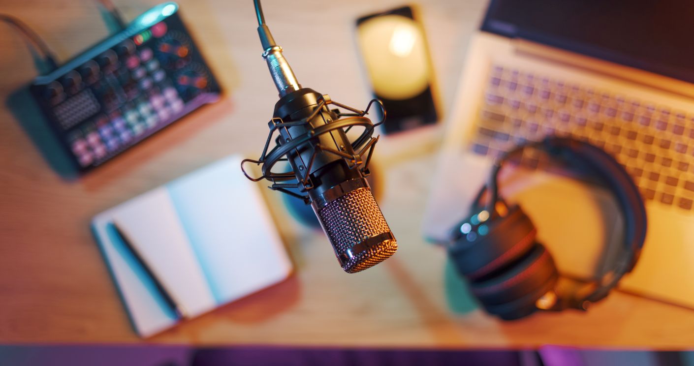 Mikrofon im Vordergrund, Laptop, Smartphone und Audioequipment auf einem Schreibtisch in einem Home-Studio, Draufsicht.