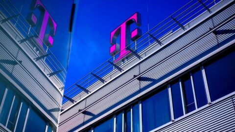 Nahaufnahme von einem Bürogebäude mit großem pinken Telekom-Logo vor blauem Himmel.