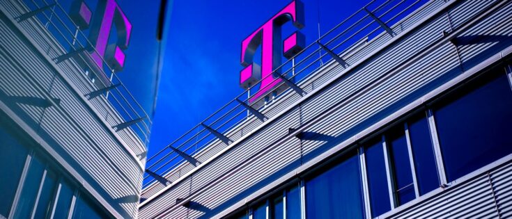 Nahaufnahme von einem Bürogebäude mit großem pinken Telekom-Logo vor blauem Himmel.
