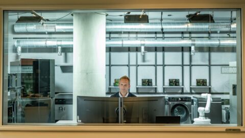 Mann sitzt vor einem Computer in einem modernen Testlabor mit Geräten im Hintergrund.