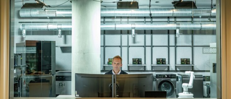 Mann sitzt vor einem Computer in einem modernen Testlabor mit Geräten im Hintergrund.