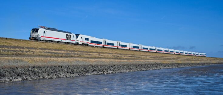 ICE L der Deutschen Bahn überquert den Hindenburgdamm, umgeben von flachem Terrain und blauem Himmel.