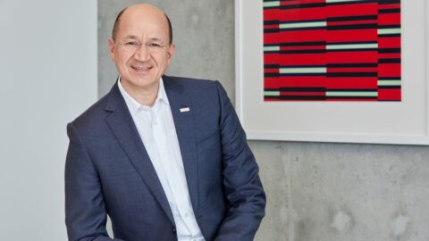 Portrait von Prof. Dr. Christof Ehrhart in Anzug, lächelnd vor einer modernen Wand mit abstrakter Kunst.