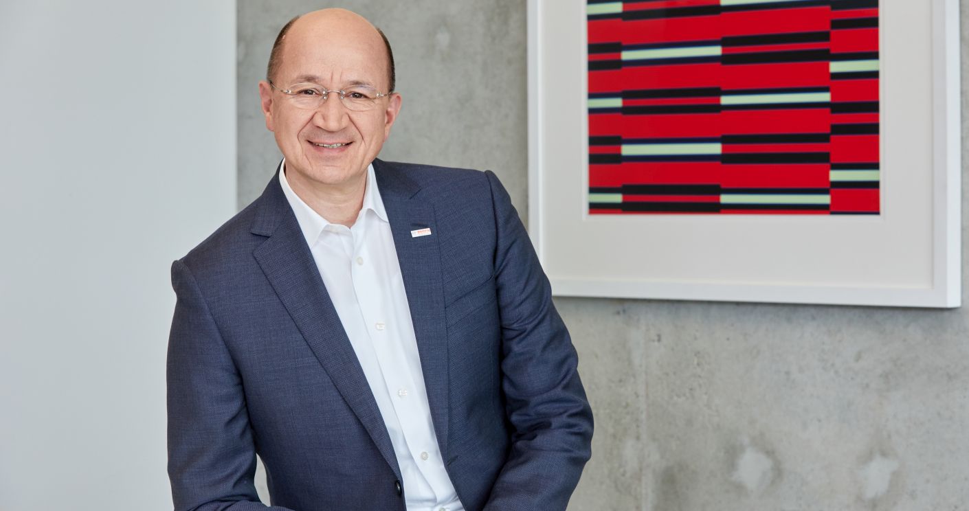 Portrait von Prof. Dr. Christof Ehrhart in Anzug, lächelnd vor einer modernen Wand mit abstrakter Kunst.