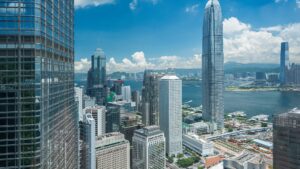 Blick auf die Skyline von Hongkong mit modernen Wolkenkratzern und dem Hafen unter einem blauen Himmel.