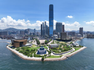 Luftaufnahme des West Kowloon Cultural Districts in Hongkong mit modernen Gebäuden und grünen Flächen am Wasser.