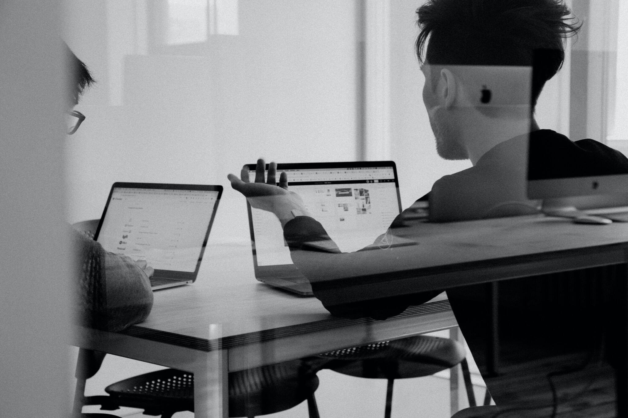 Zwei Personen sitzen an einem Tisch mit Laptops und diskutieren, der Raum ist hell und modern gestaltet.